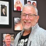 a man smiling in front of a wall of pictures