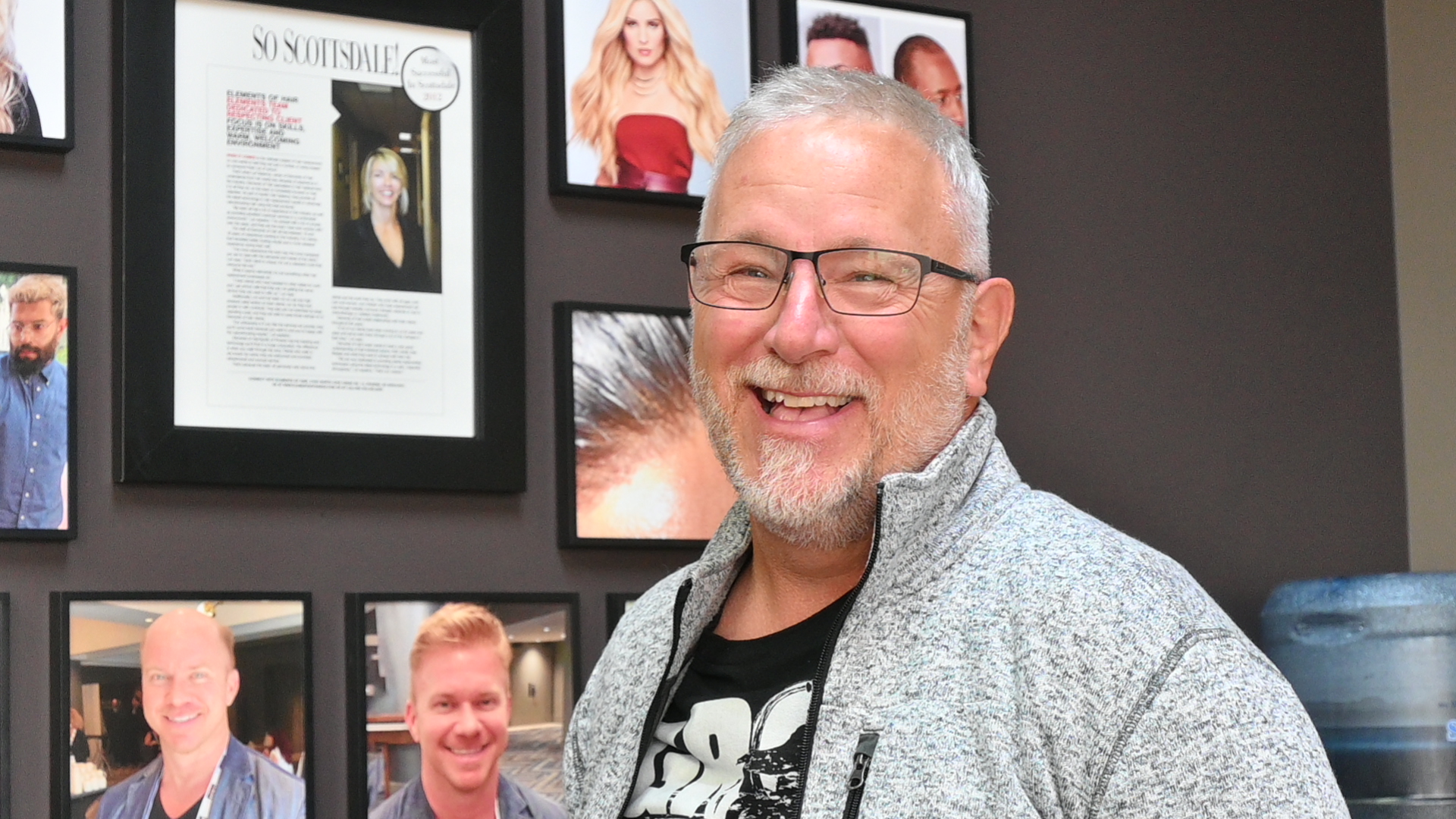 a man smiling in front of a wall of pictures
